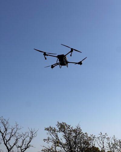 Doss Drone Services agricultural spray drone in flight against clear blue East Texas sky during precision spraying operation