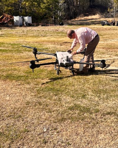 FAA certified Doss Drone Services technician preparing large agricultural spray drone for field operation in East Texas